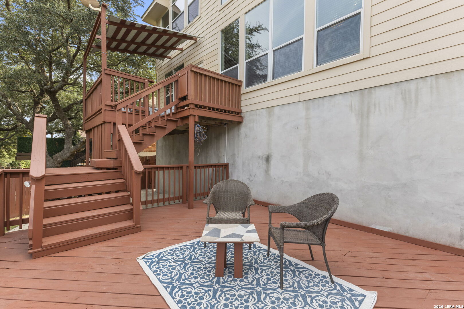 Furnished deck with stairs, pergola, wicker seating, and a patterned rug beside the home.