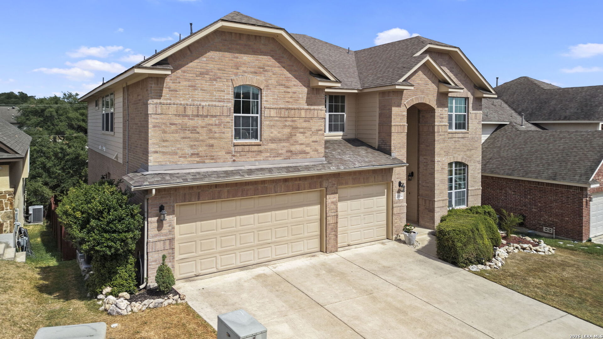 Two-story brick home with a broad driveway, two garage doors, and an arched entry.