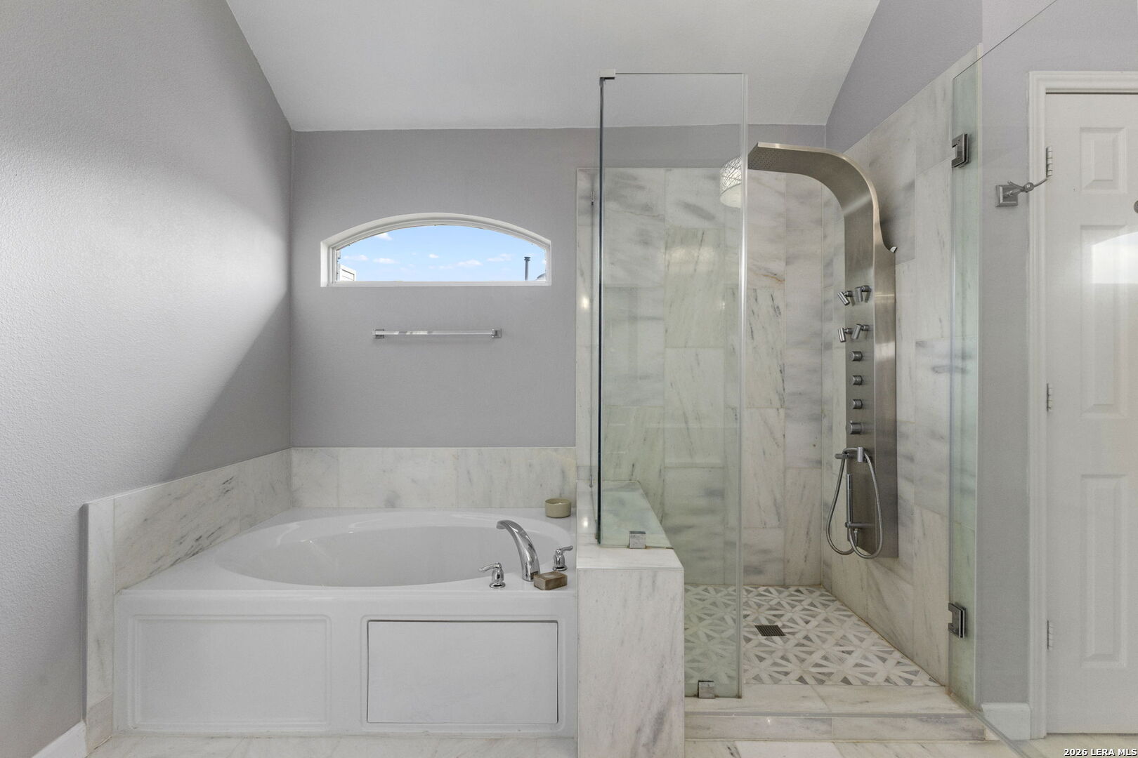 Bathroom with a built-in soaking tub beside a glass-enclosed marble shower with patterned floor tile.