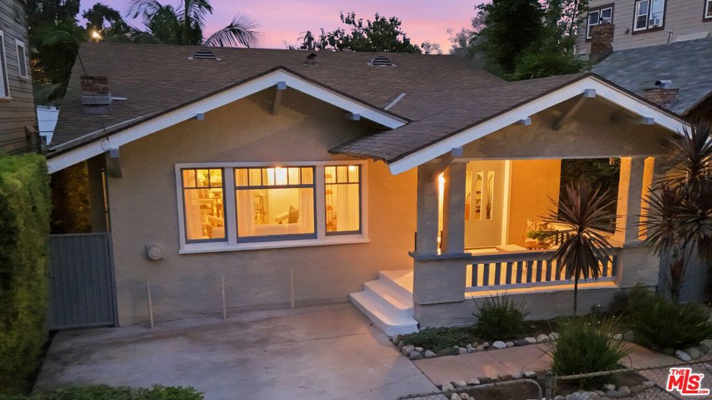 Single-story home with a covered front porch, warmly lit windows, and a concrete driveway at dusk.