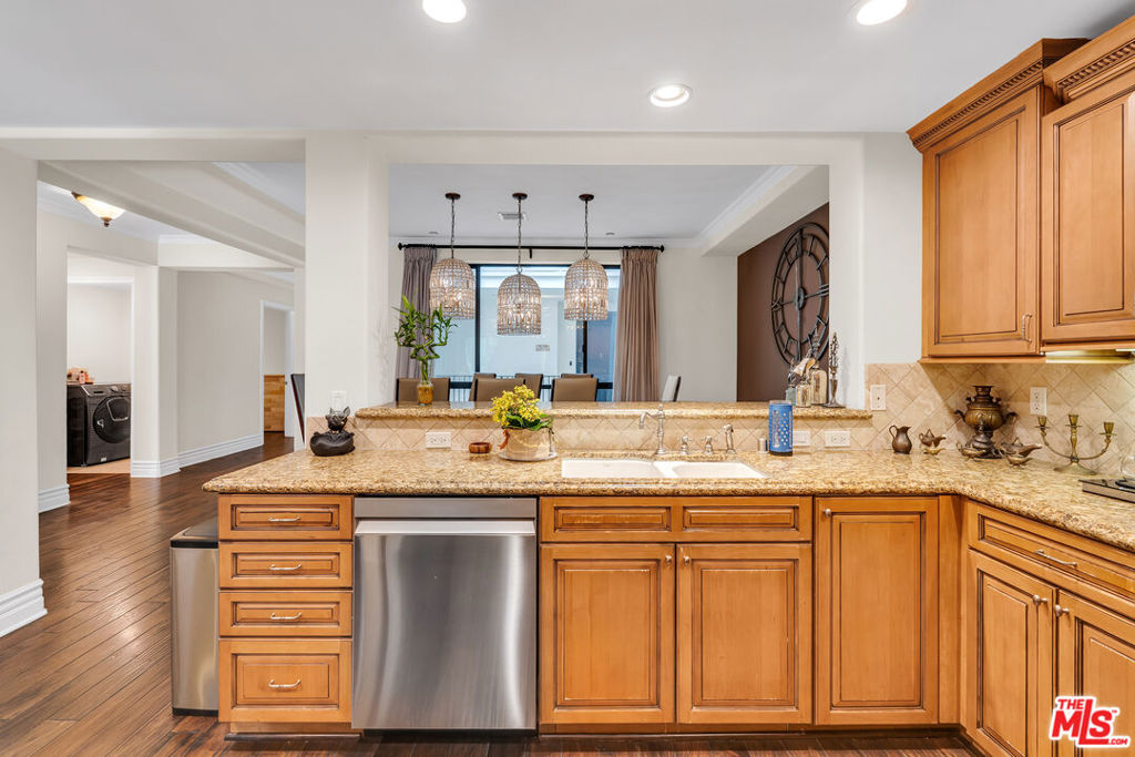 Kitchen with warm wood cabinets, granite counters, and a stainless-steel dishwasher opening to a dining area.