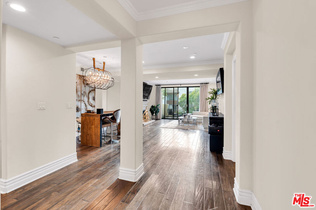 Condo hallway opening to a living and dining area with wood-look floors and balcony doors.
