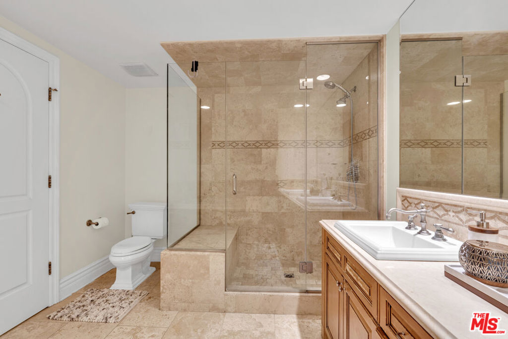 Bathroom with a glass-enclosed beige stone shower and wood vanity.