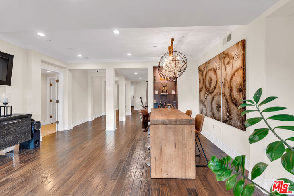 Dining area with a long wooden table, sculptural chandelier, and dark wood-look flooring.