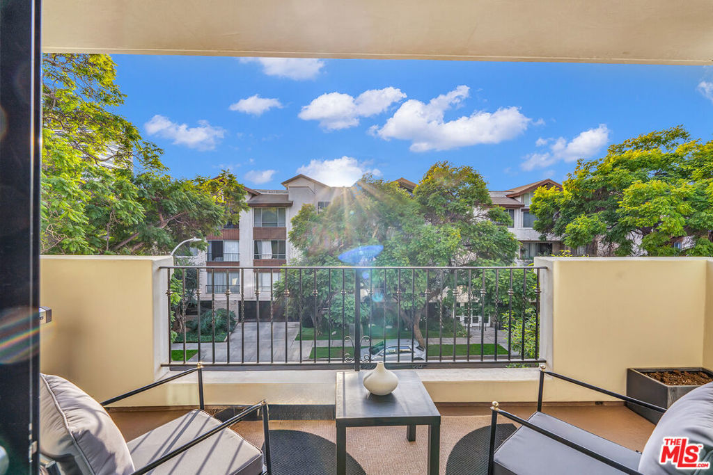 Apartment balcony with cushioned seating overlooks a landscaped courtyard and neighboring buildings.