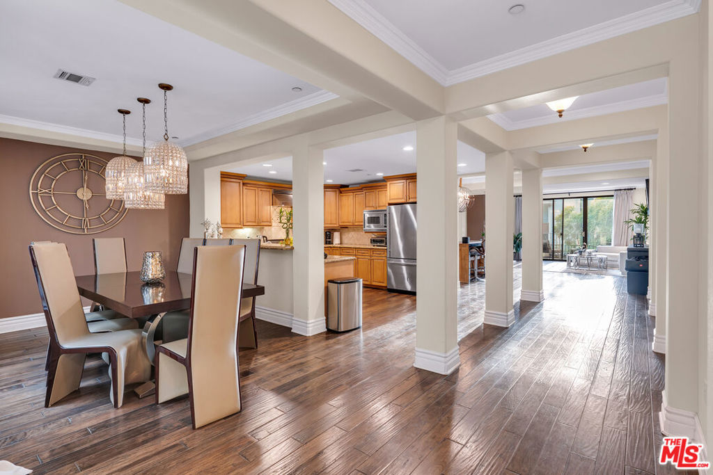 Open-plan dining area with crystal chandeliers, wood floors, and kitchen and living areas beyond.