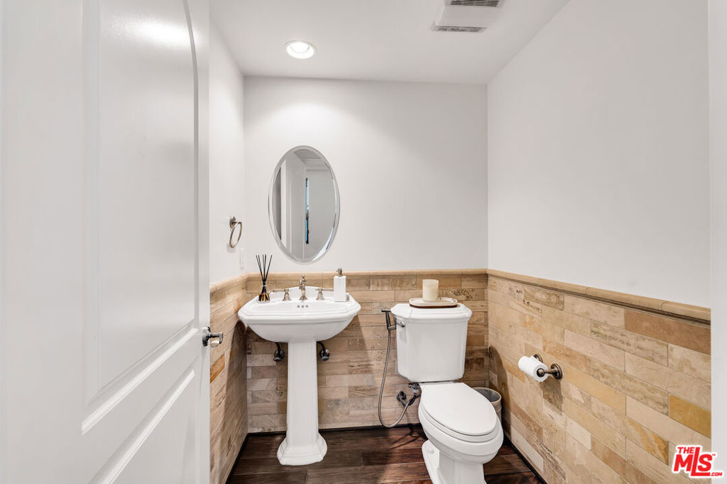 Bathroom with a pedestal sink, oval mirror, and tan stone-tile walls.