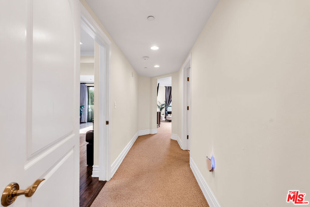 Carpeted condominium hallway with white walls, recessed lights, and open doorways.