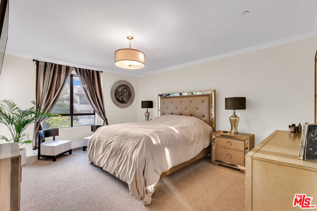 Furnished bedroom with a large bed, tufted mirrored headboard, and window framed by dark curtains.