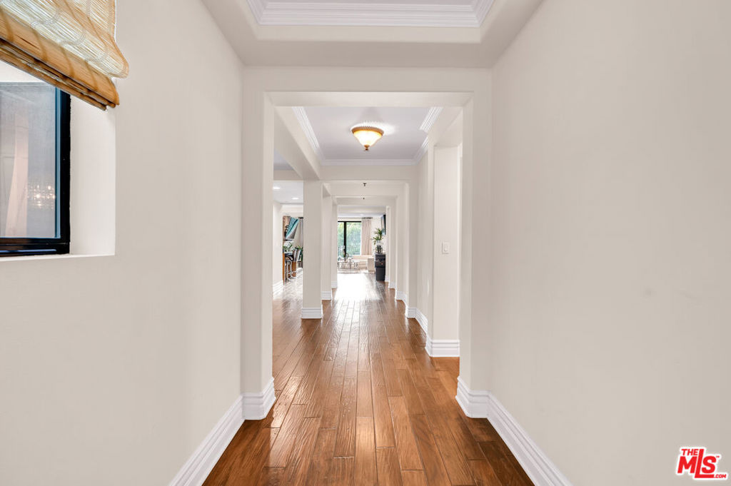 Long hallway with polished hardwood floors, decorative ceiling molding, and a woven shade over the window.