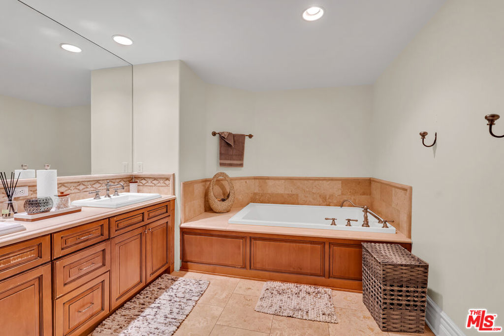 Bathroom with built-in soaking tub, wood vanity, and tan tile accents.