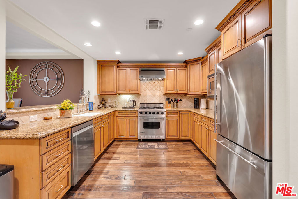 Kitchen with honey-toned cabinetry, granite counters, stainless steel appliances and wood-look flooring.