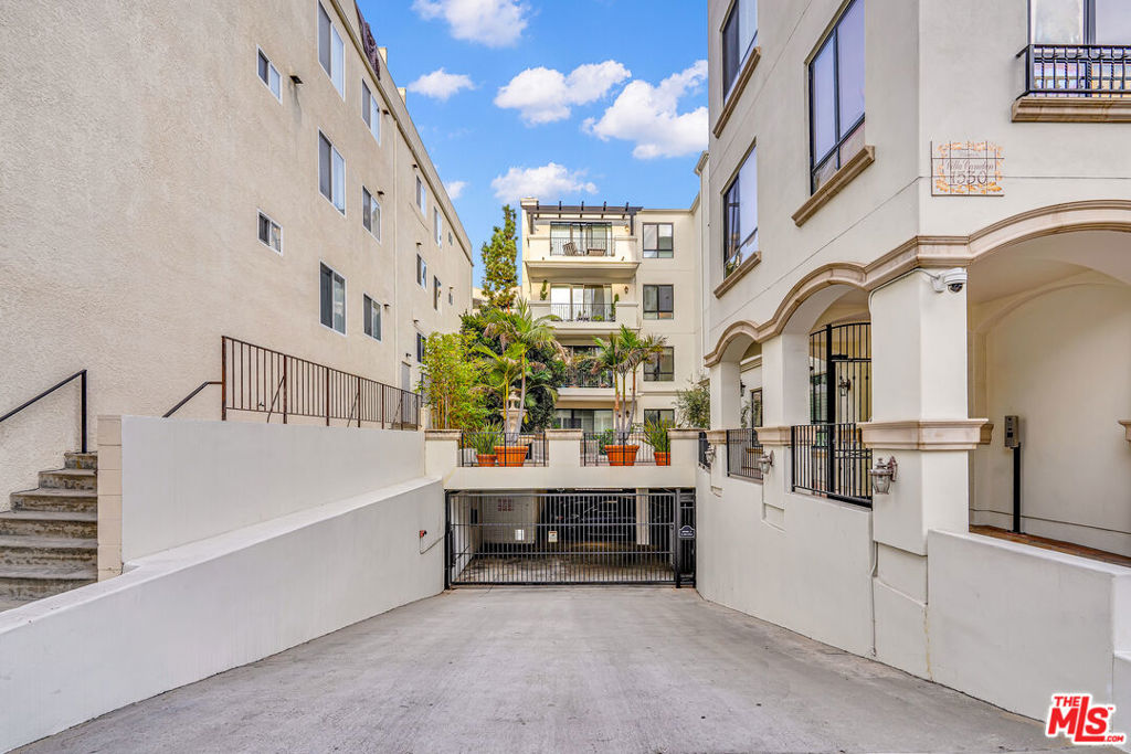 Apartment building entrance with a sloped driveway leading to a gated underground garage.