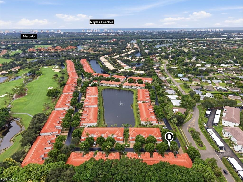Aerial view of red-roofed condominiums beside lakes and a golf course, with Naples Beaches on the horizon.