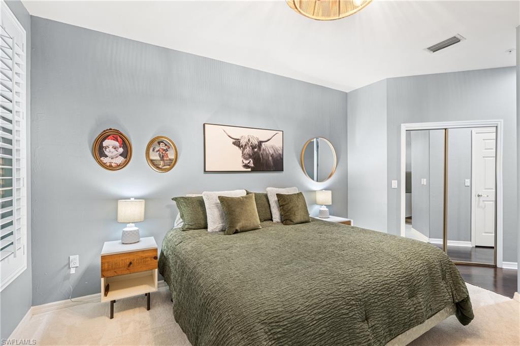 Bedroom with a green-covered king-size bed, framed art, round mirror, and mirrored closet doors.