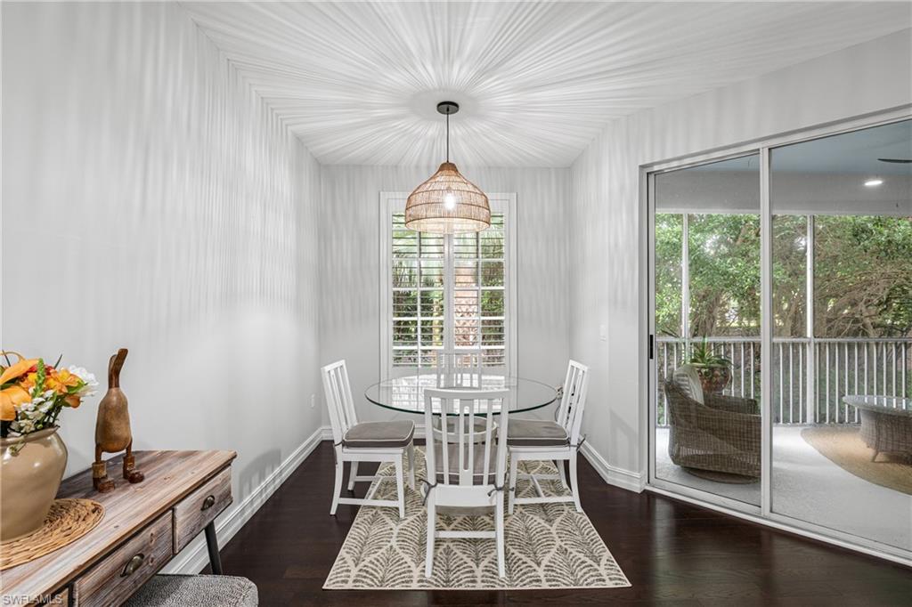 Dining room with a glass table, white chairs, woven pendant light, and sliding doors to a screened lanai.