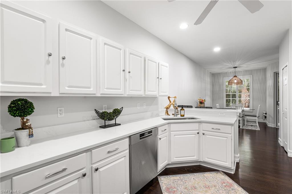 White kitchen with paneled cabinets, stainless steel dishwasher, and dining area by a window.