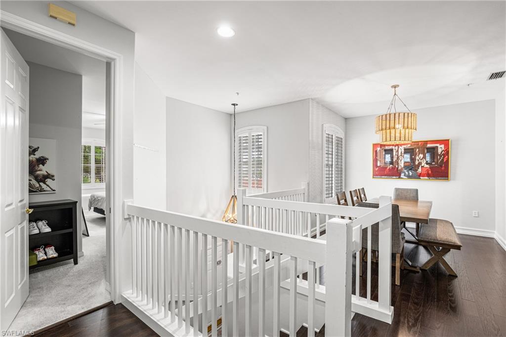 Dining area with a wood table beside a white stair railing and shuttered windows.