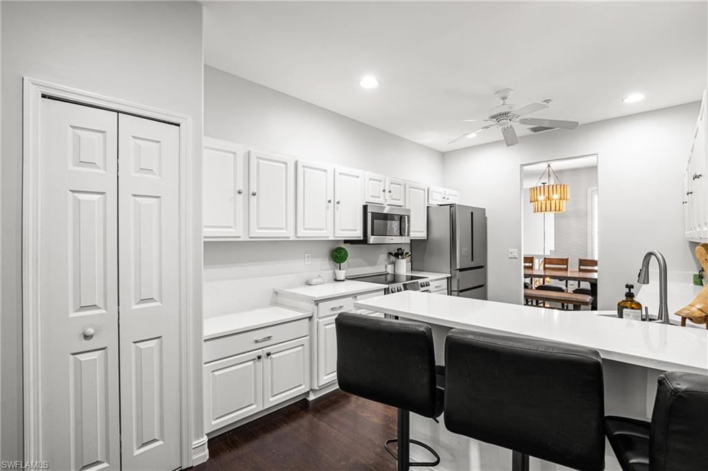 Kitchen with white cabinets, stainless appliances, and a large island with black bar stools.