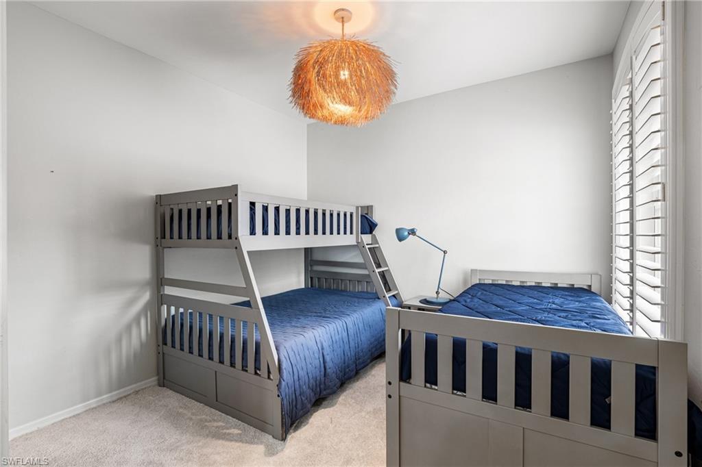 Bedroom with gray bunk and twin beds, blue quilts, a blue lamp, and plantation shutters.