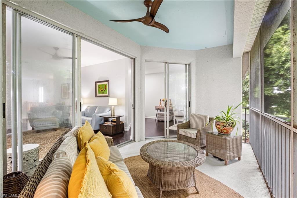 Screened lanai with wicker seating, yellow pillows, and views of trees.