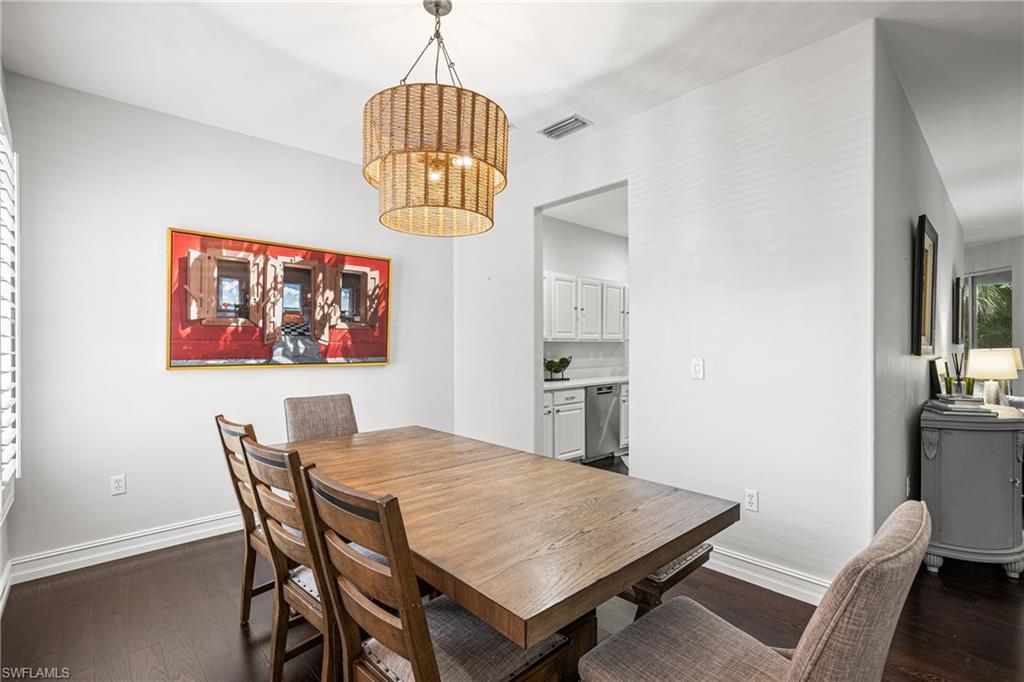 Dining room with a large wood table, woven pendant light, and colorful wall art.
