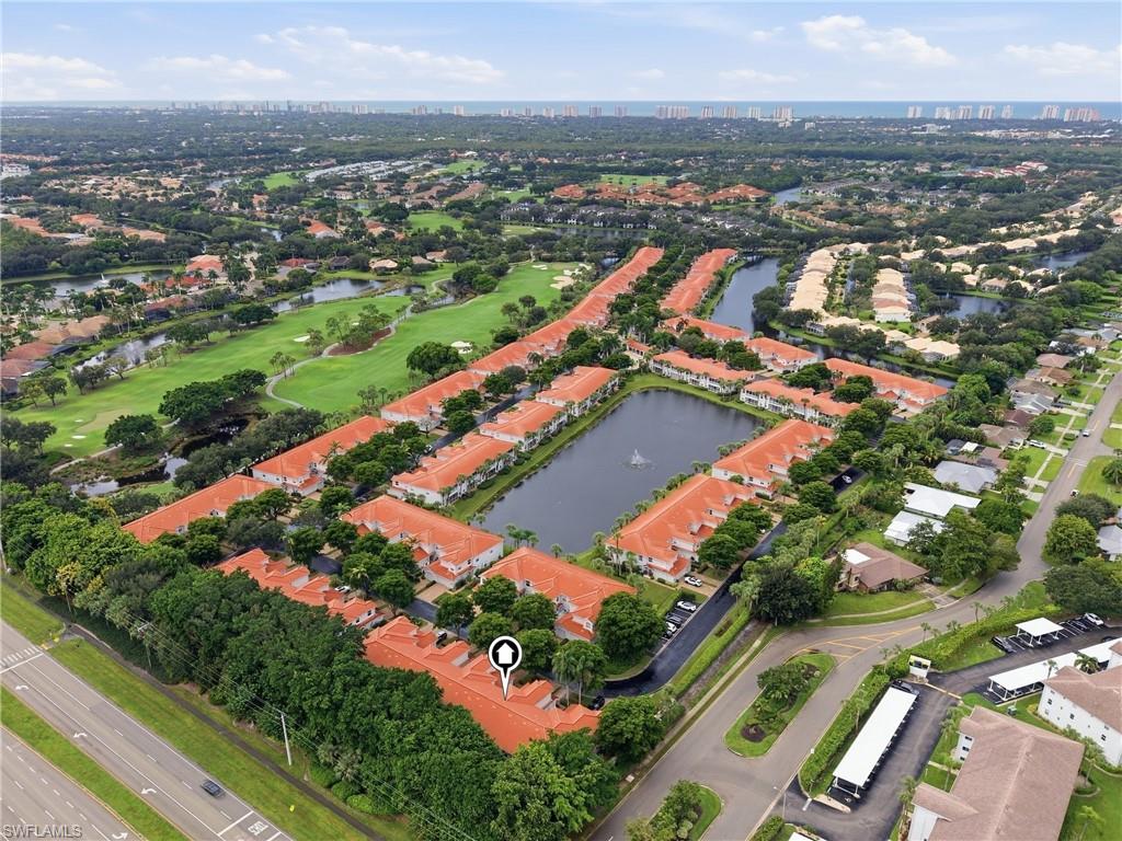 Aerial view of red-roofed condominiums surrounding a pond, with a golf course and distant high-rises.