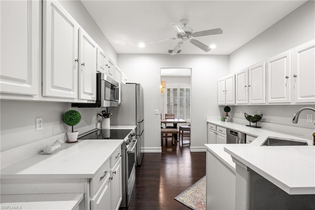 Bright white kitchen with shaker cabinets, stainless steel appliances, and dark wood floors.