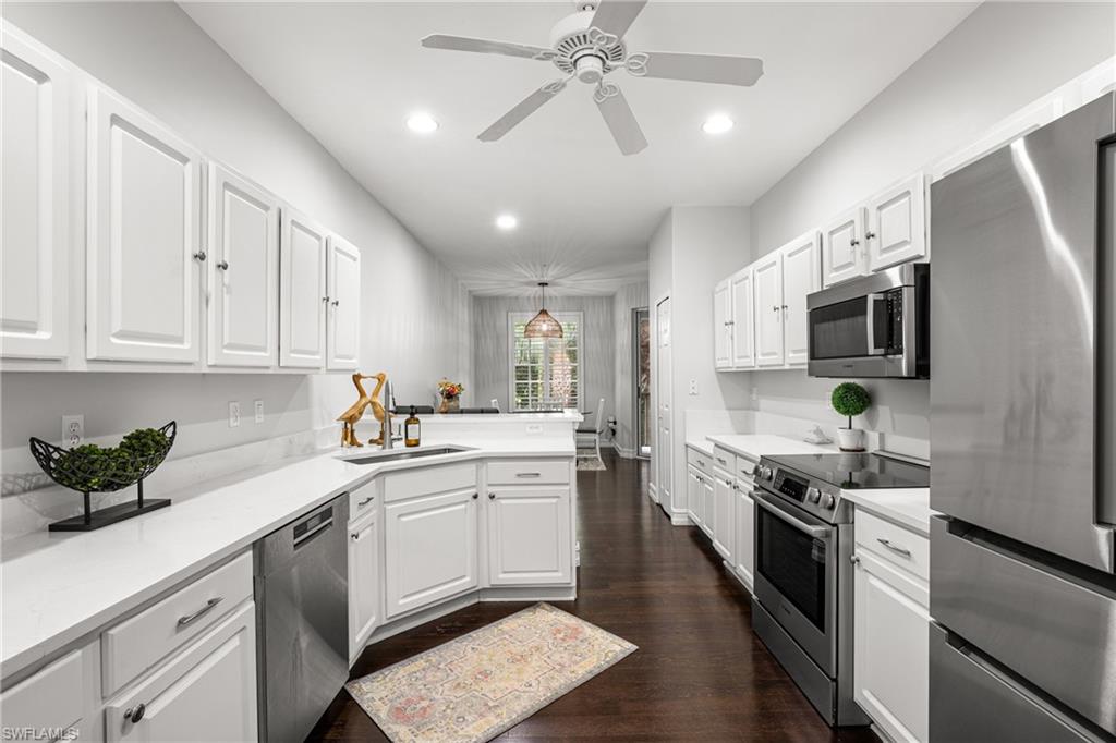 Galley kitchen with white shaker cabinets, stainless steel appliances, and a central island with sink.