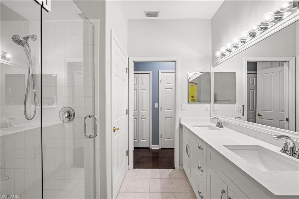 Bathroom with a glass shower and long double-sink vanity beneath large mirrors.