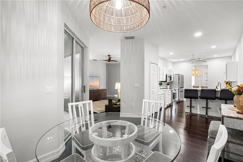 Dining area with a round glass table, opening onto a bright kitchen and breakfast bar.