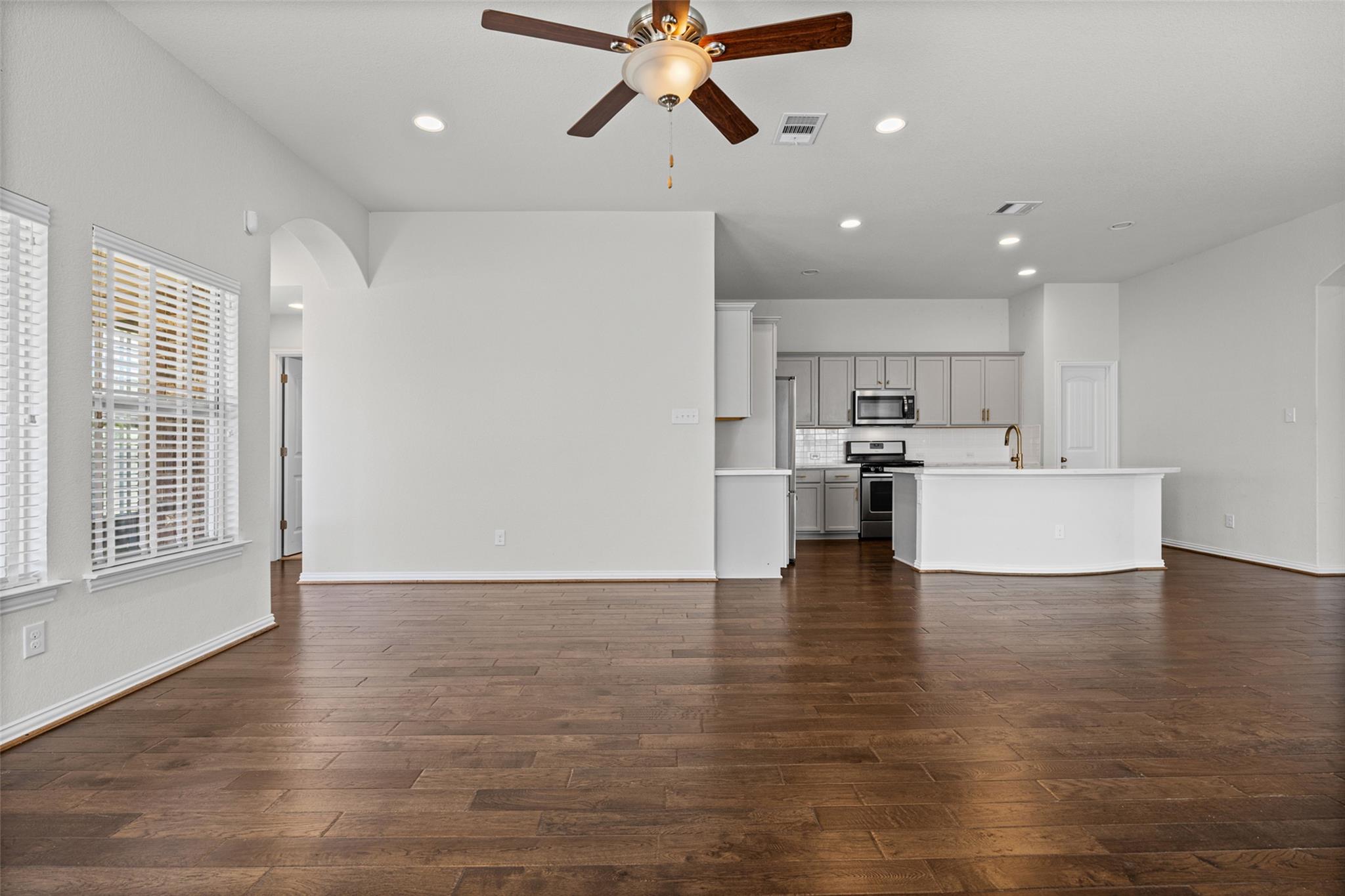 Open-plan living area and kitchen with dark wood floors, gray cabinets, and a white peninsula.