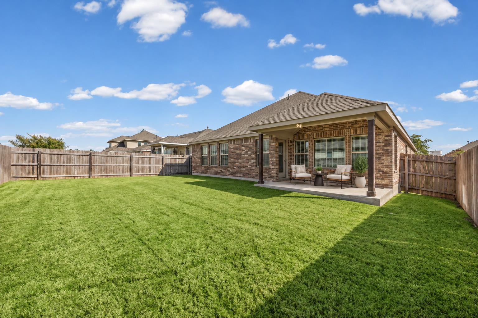 Brick house with a covered patio overlooking a large fenced lawn.