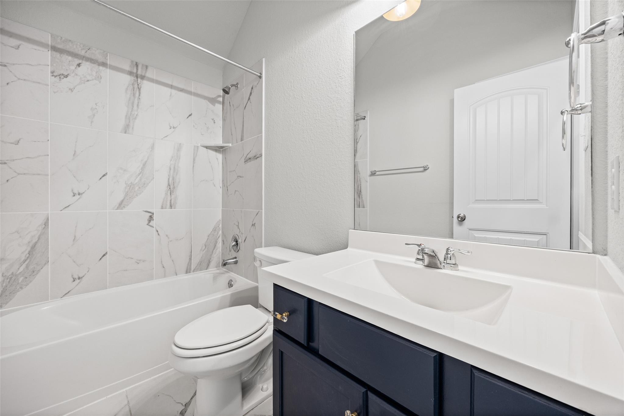 Bathroom with marble-look tub surround and dark blue vanity.