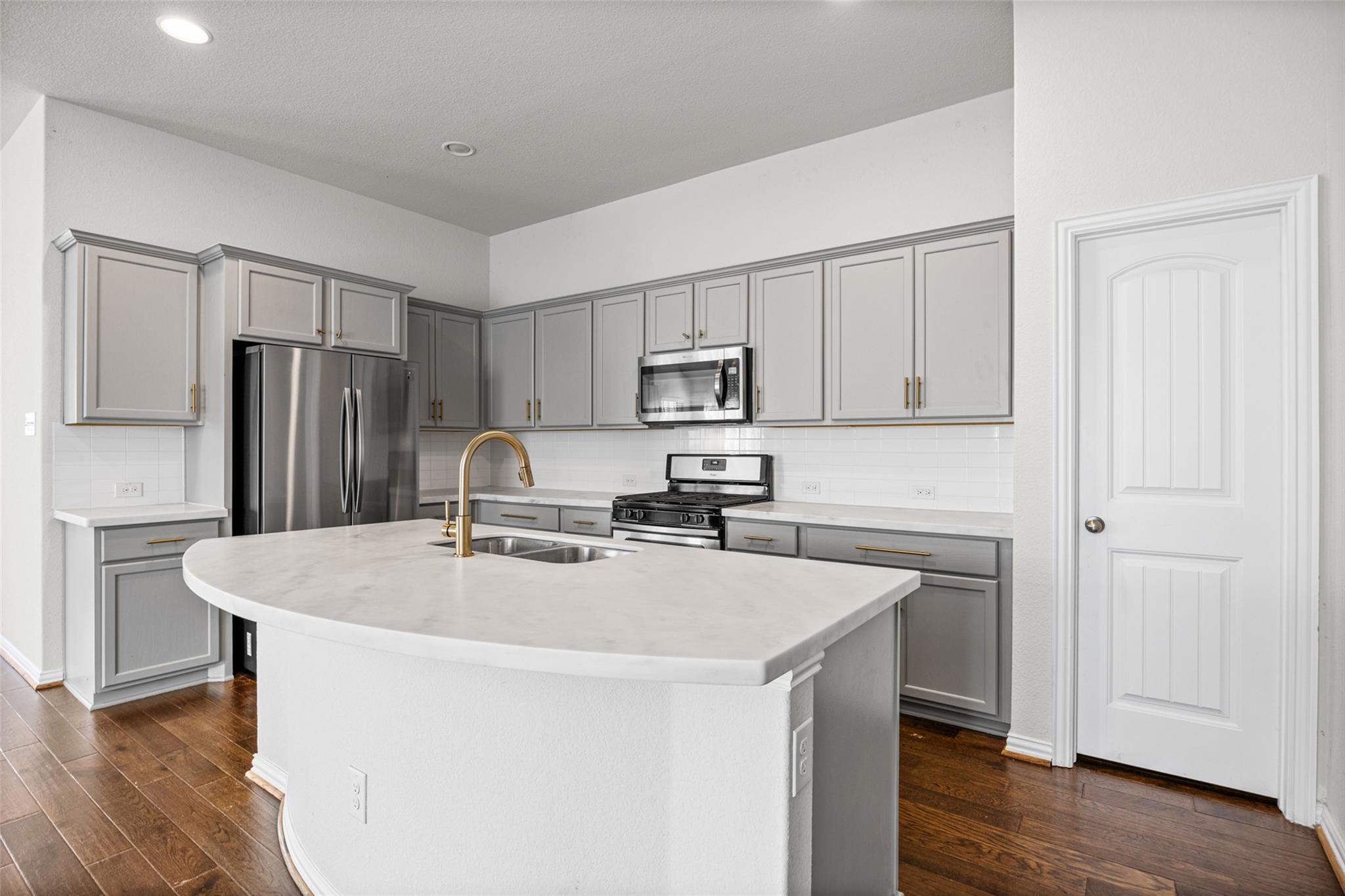 Kitchen with gray cabinets, stainless appliances, and a large white island with a gold faucet.