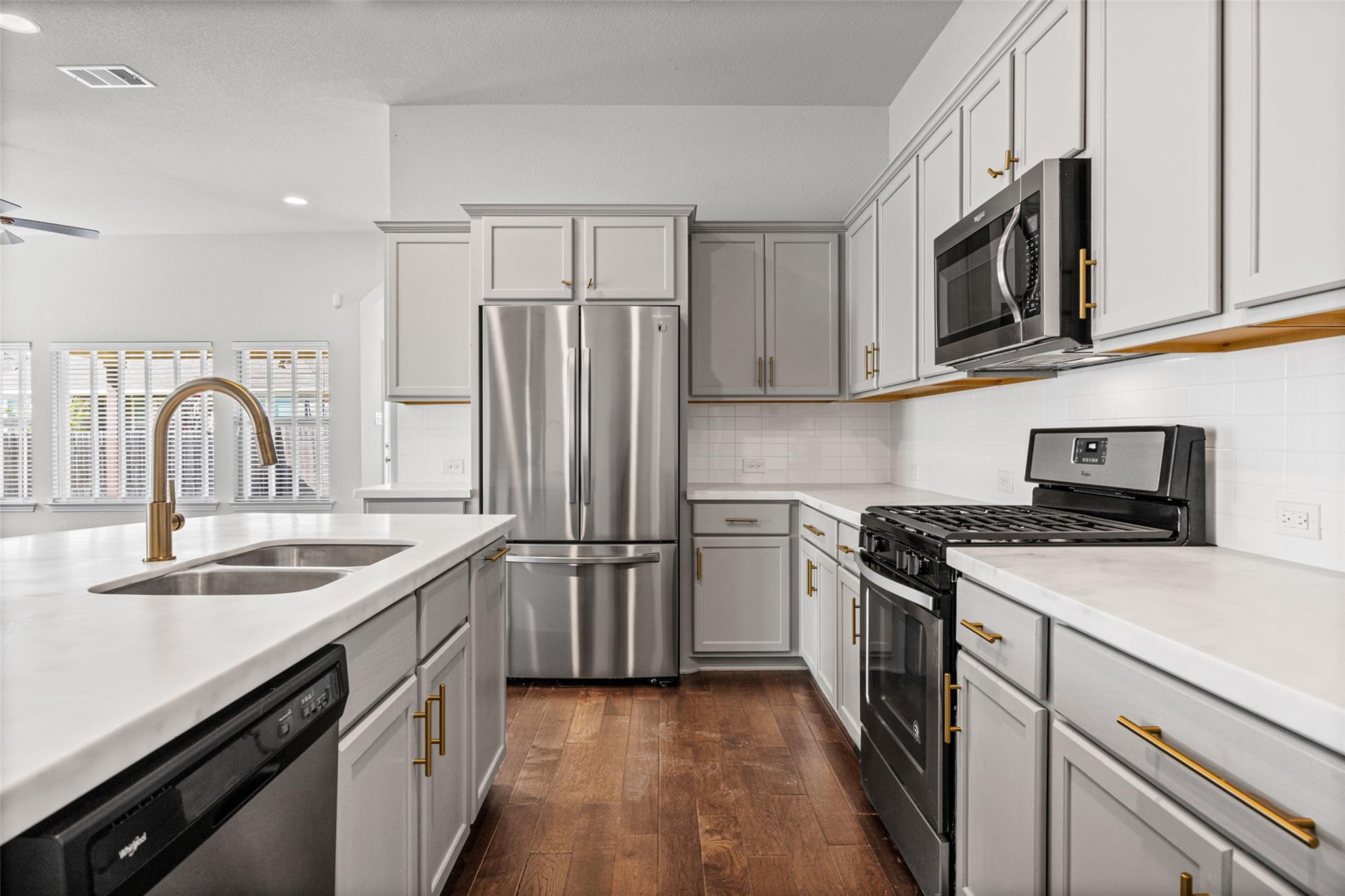 Kitchen with white cabinets, brass hardware, stainless appliances, and a large island sink