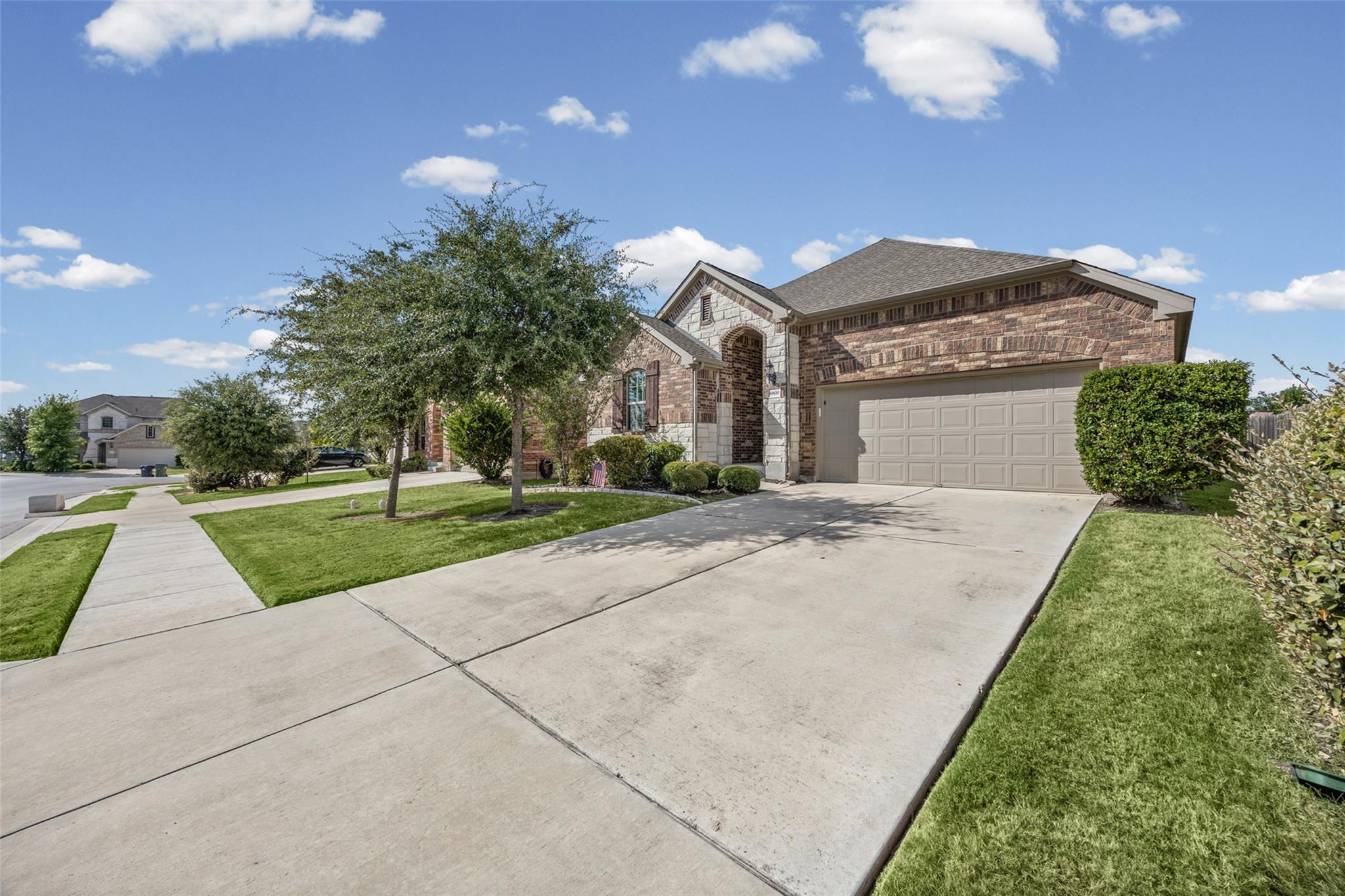 Brick-and-stone house with a two-car garage, wide driveway, and landscaped front lawn.