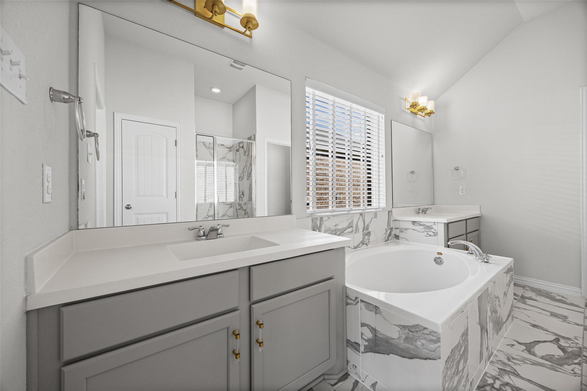 Primary bathroom with a gray double vanity, soaking tub, and marble-patterned tile.