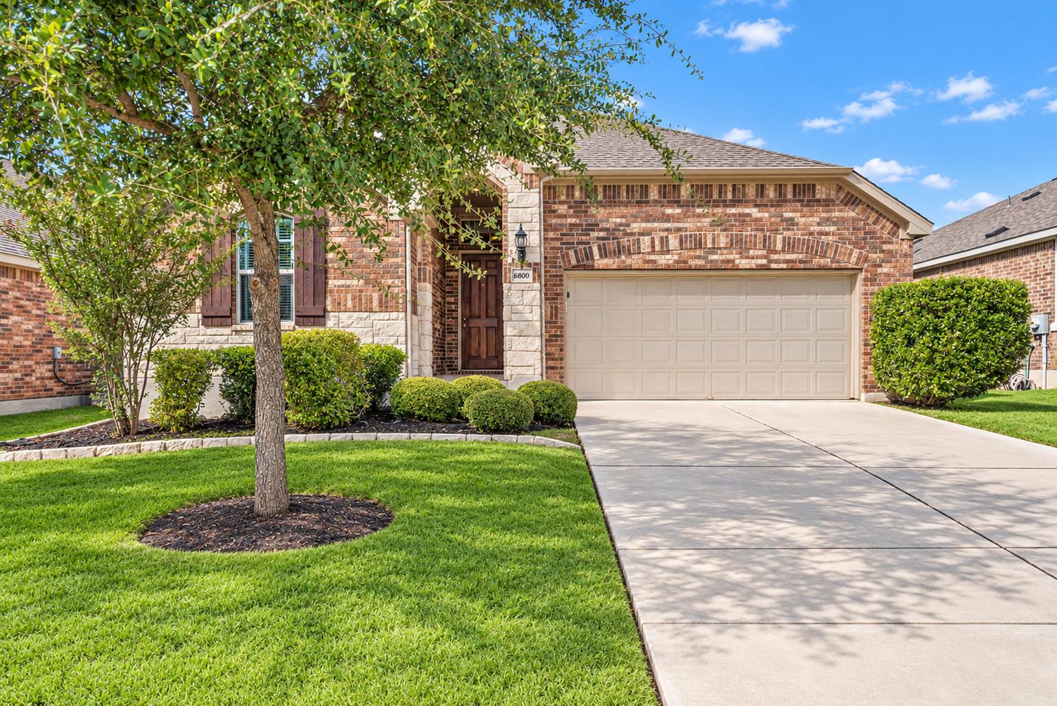 Brick home with an attached two-car garage, landscaped front lawn, and concrete driveway.