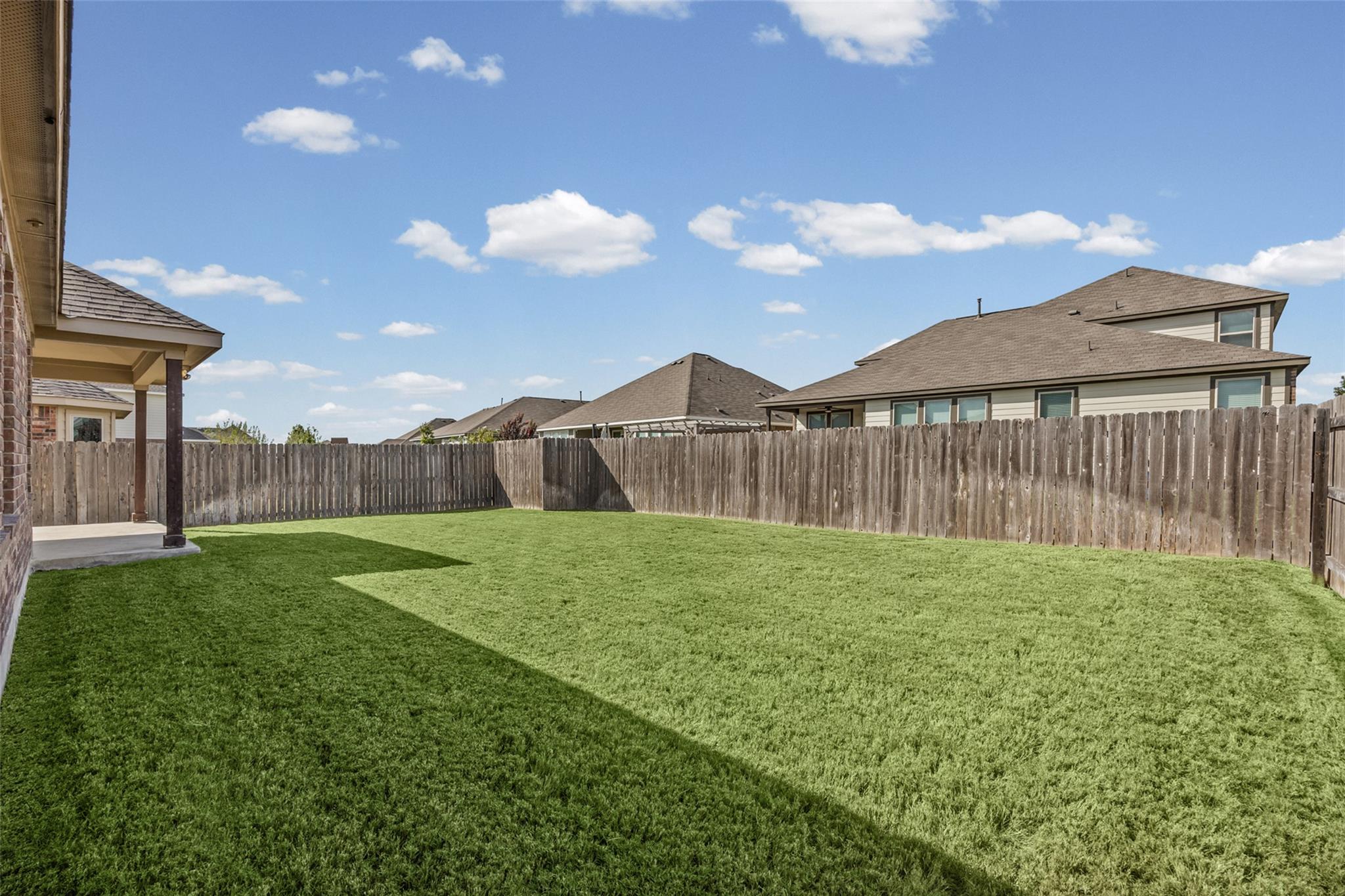 Fenced backyard with a broad green lawn and covered patio beside the home.
