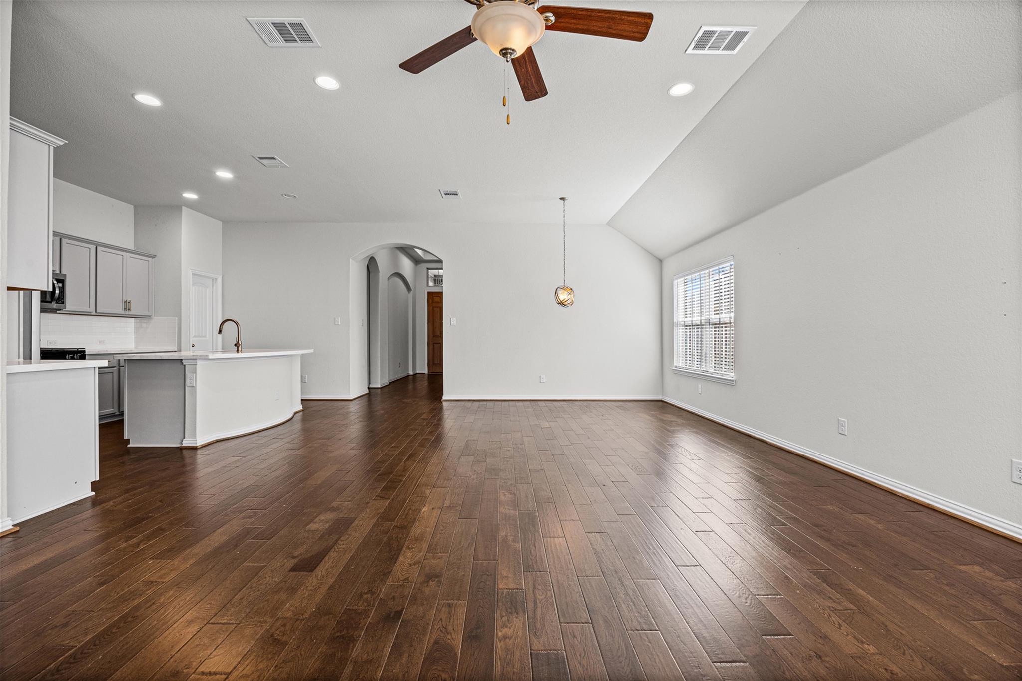 Open living and dining area with dark hardwood floors, vaulted ceiling, and kitchen peninsula.