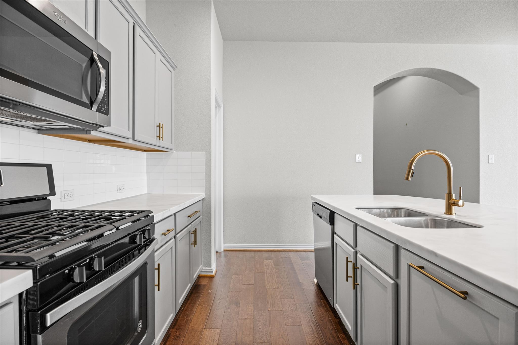 Vacant kitchen with white cabinetry, a gas range, and an island with a double sink and brass faucet.