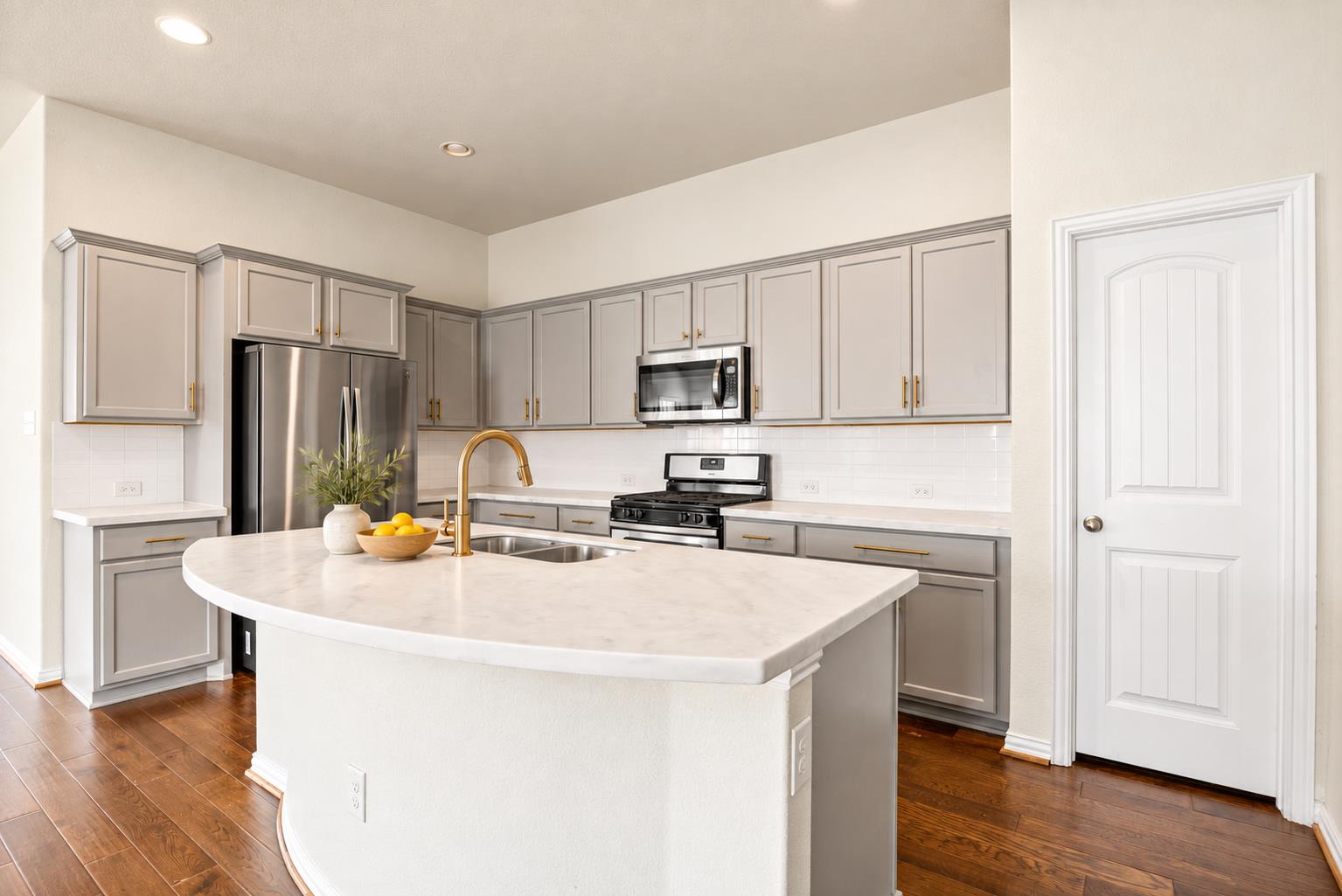 Modern kitchen with gray cabinets, stainless appliances, and a large white island with a curved breakfast bar.