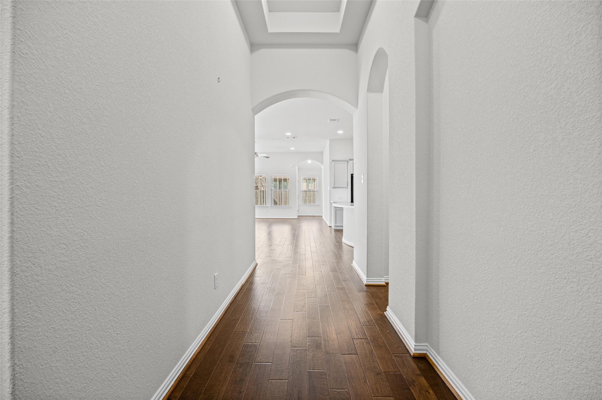 Empty hallway with dark wood-look tile flooring and arched openings leading to a bright adjoining room.