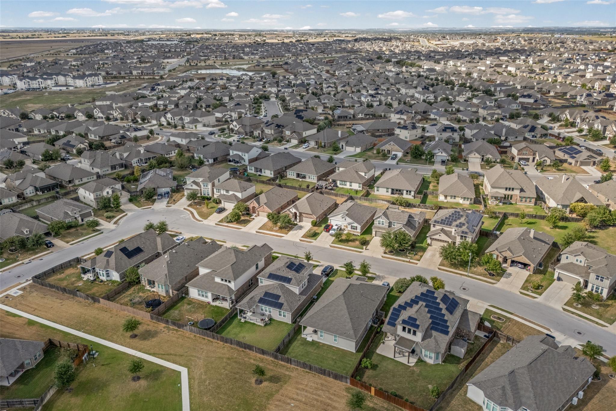 Aerial view of a sprawling subdivision with curving streets and solar panels on several rooftops.