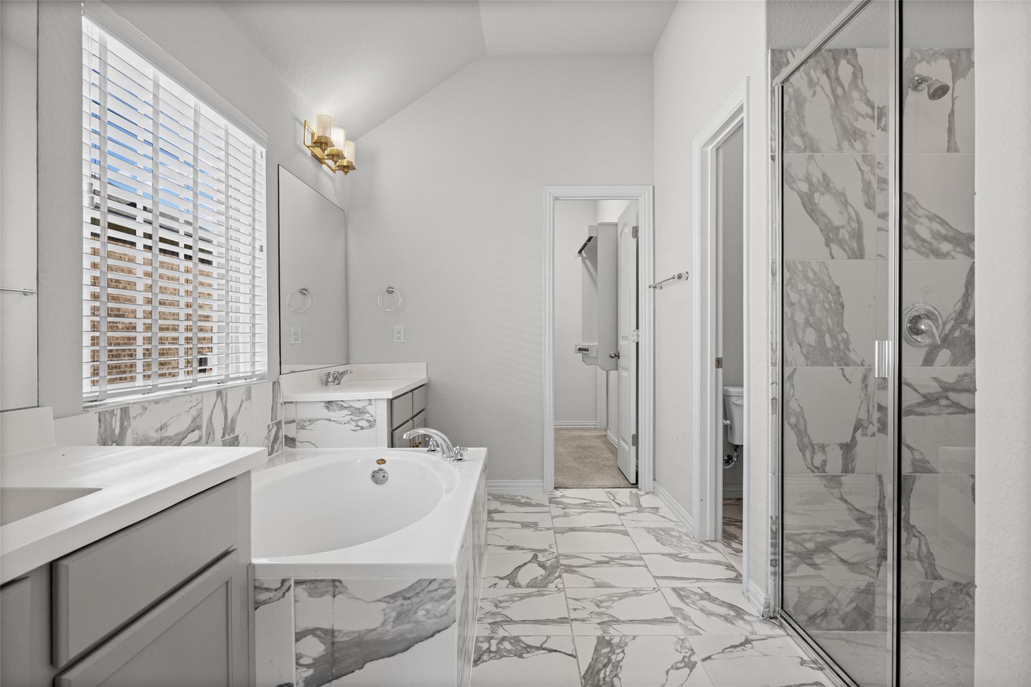 Bright bathroom with a soaking tub and marble-patterned tile beside a glass-enclosed shower.