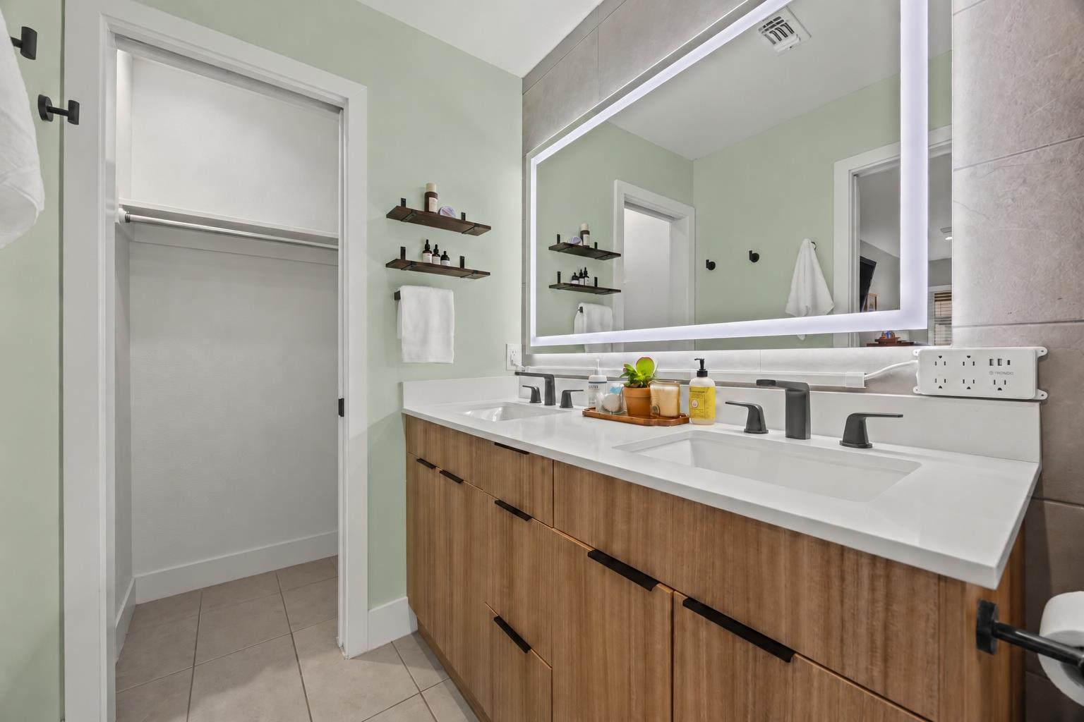 Bathroom with a double-sink vanity, wood cabinetry, and a large illuminated mirror.