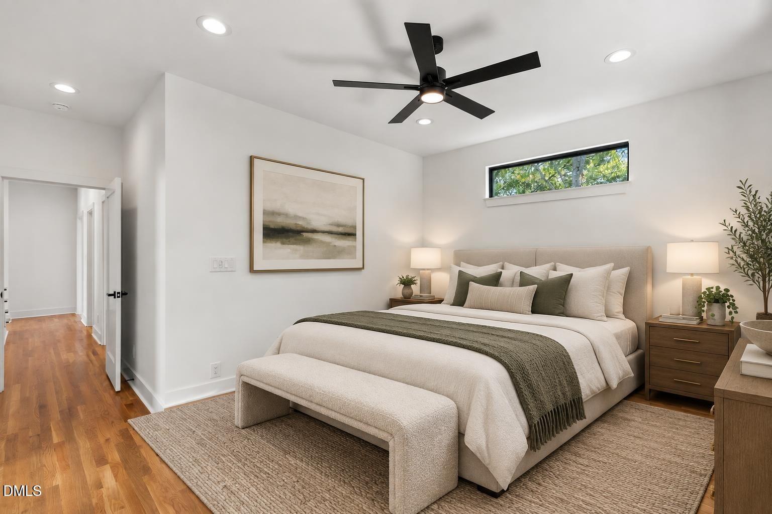 Staged bedroom with an upholstered bed, bench, black ceiling fan, and narrow high window.