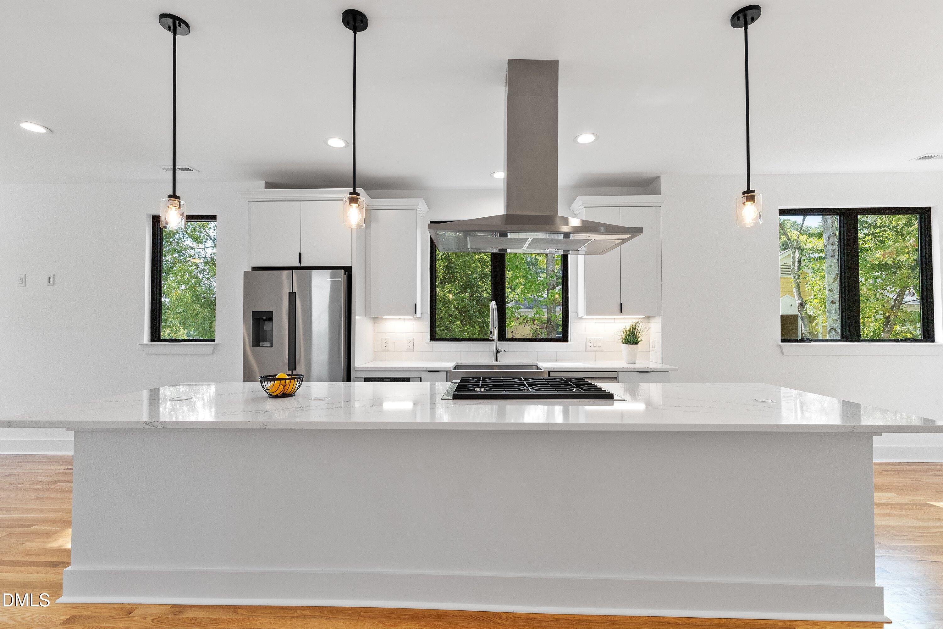 Modern white kitchen with a large quartz island, gas cooktop, and stainless steel appliances.