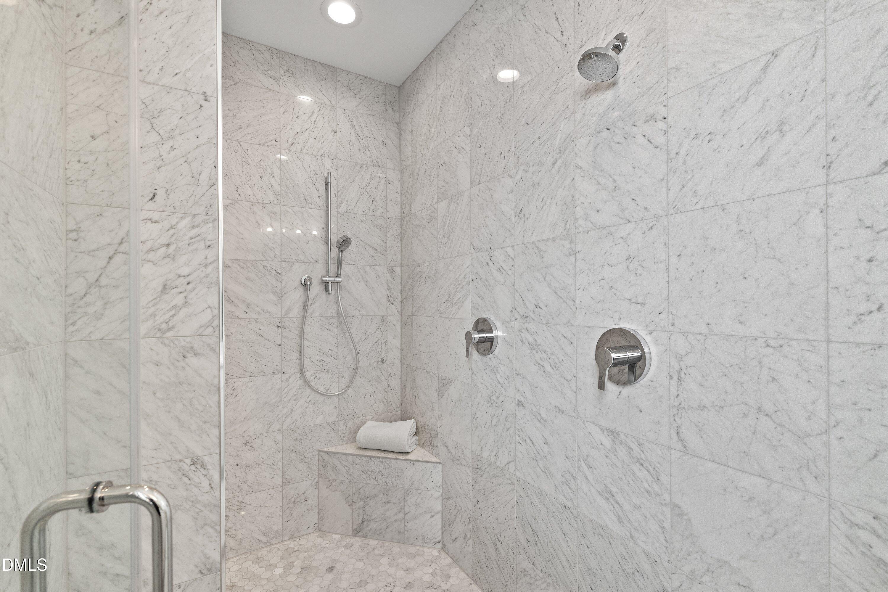 Marble walk-in shower with a glass enclosure, dual showerheads, and a built-in bench.